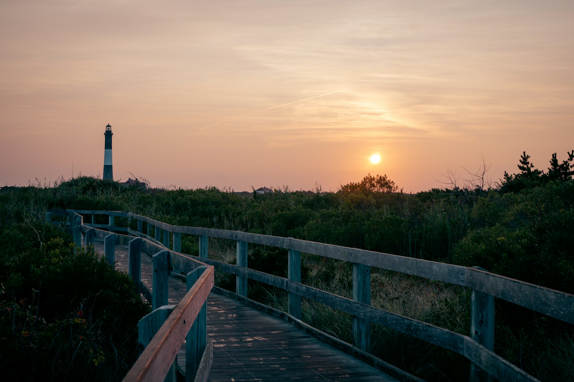 A wooden walkway leading to a lighthouse at sunset