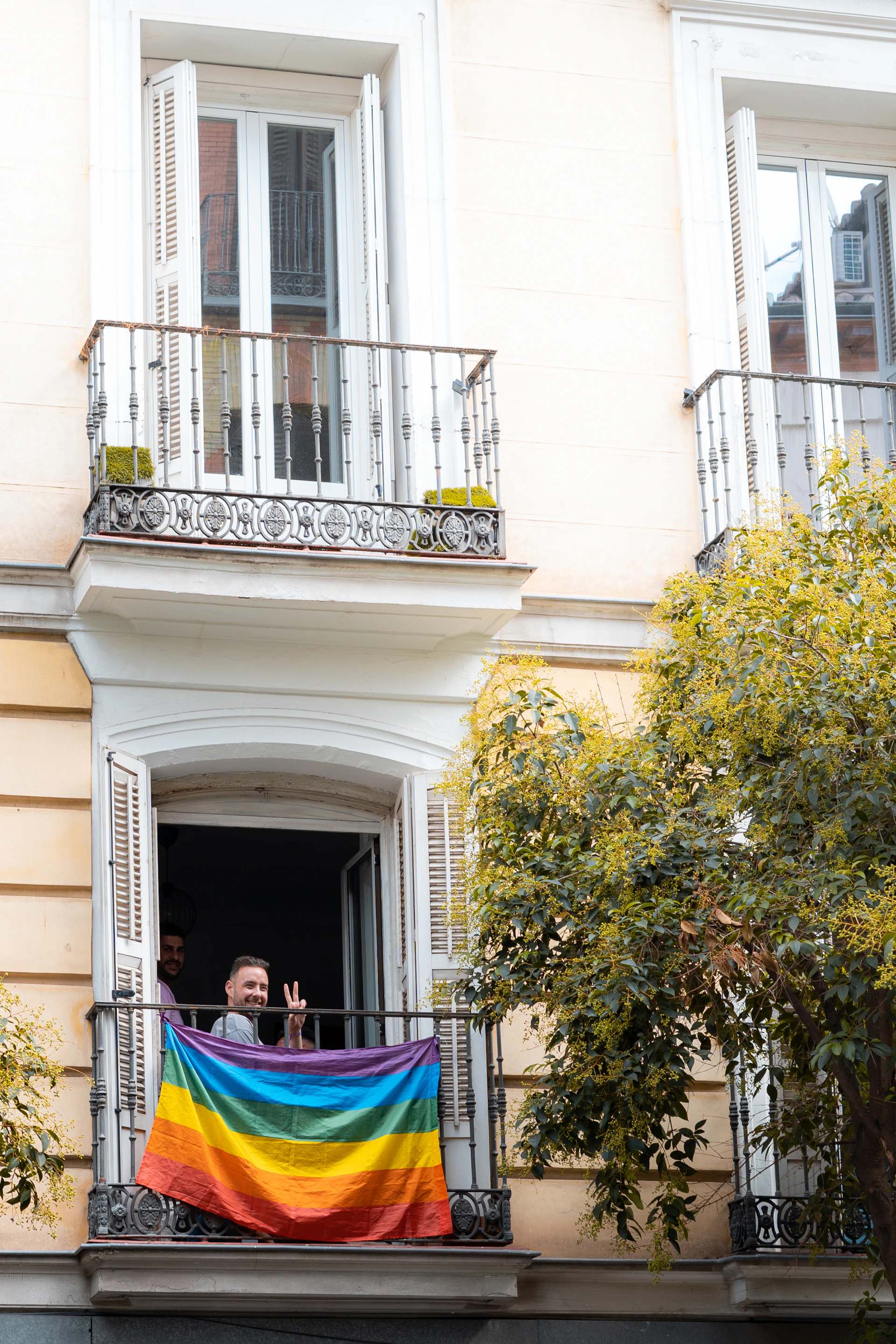 A man standing on a balcony holding a rainbow flag