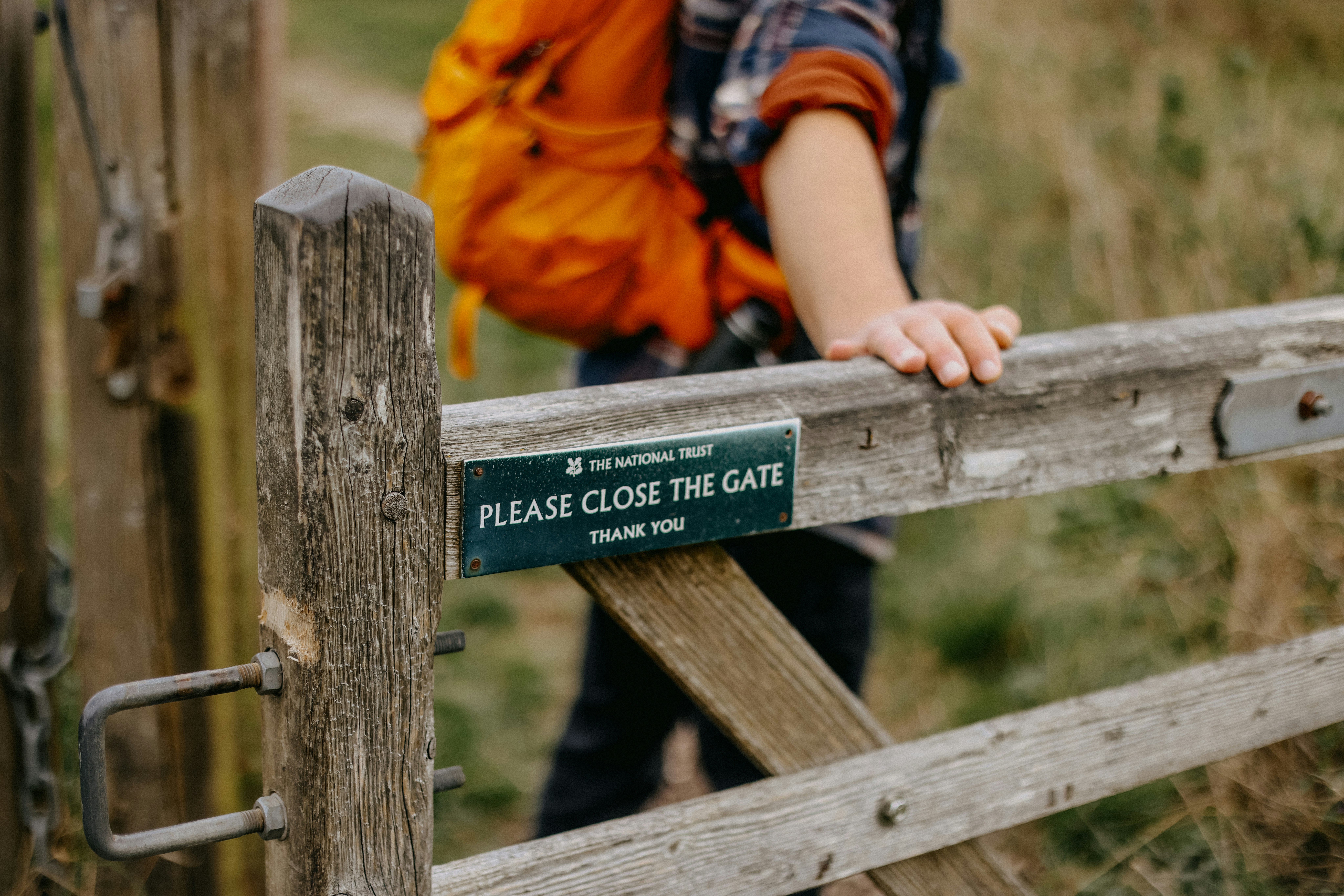 A person with a backpack is leaning on a fence