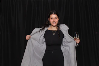 A woman holding a glass of wine in front of a black backdrop