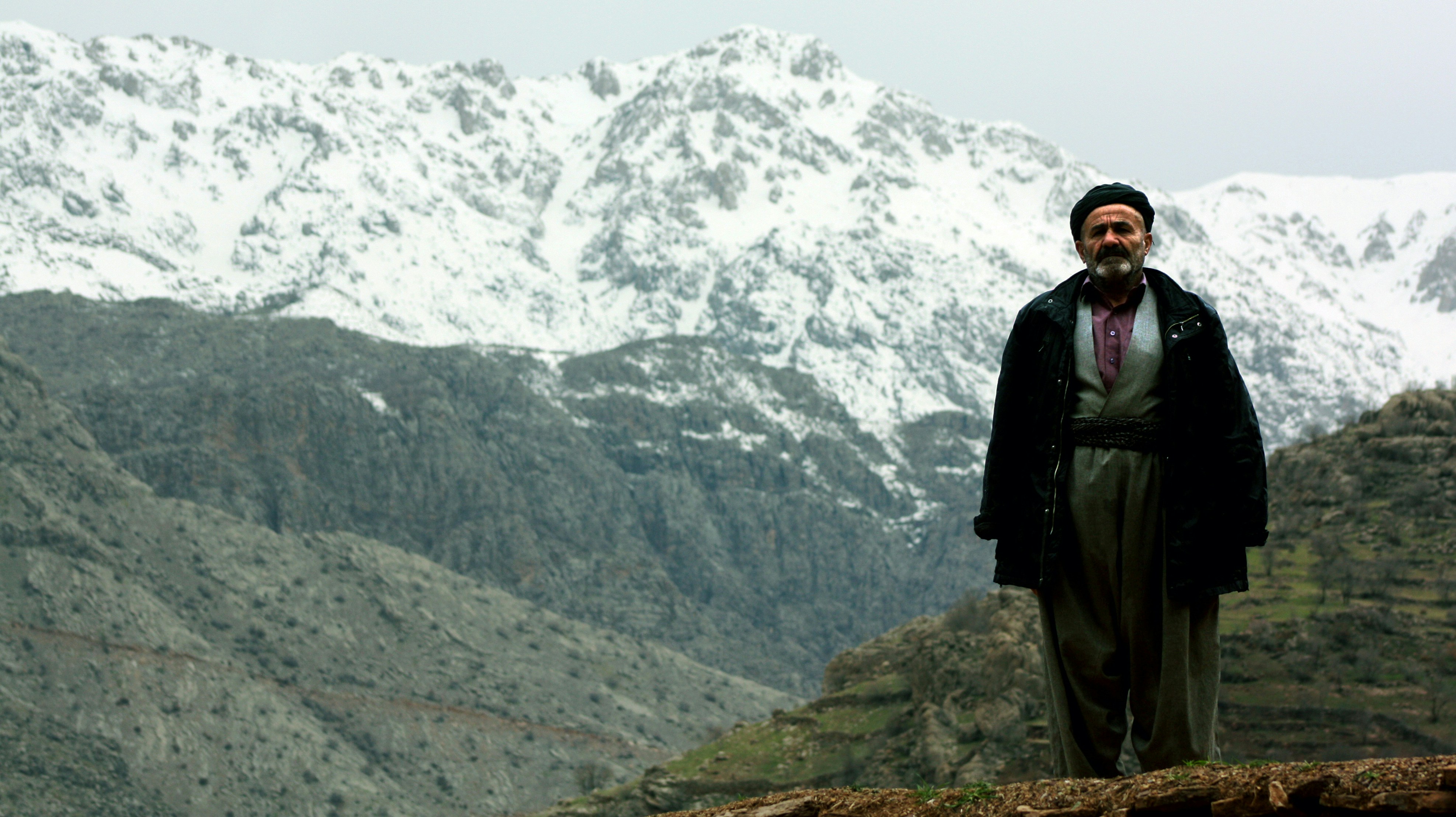 A man standing on top of a mountain with snow covered mountains in the background