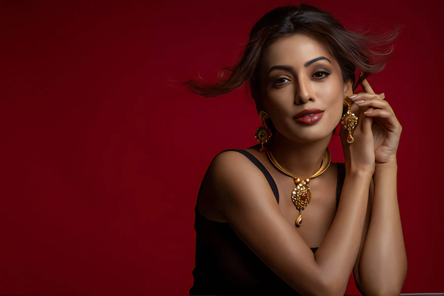 Adult woman against a deep red backdrop wearing a gold collar necklace and statement earrings