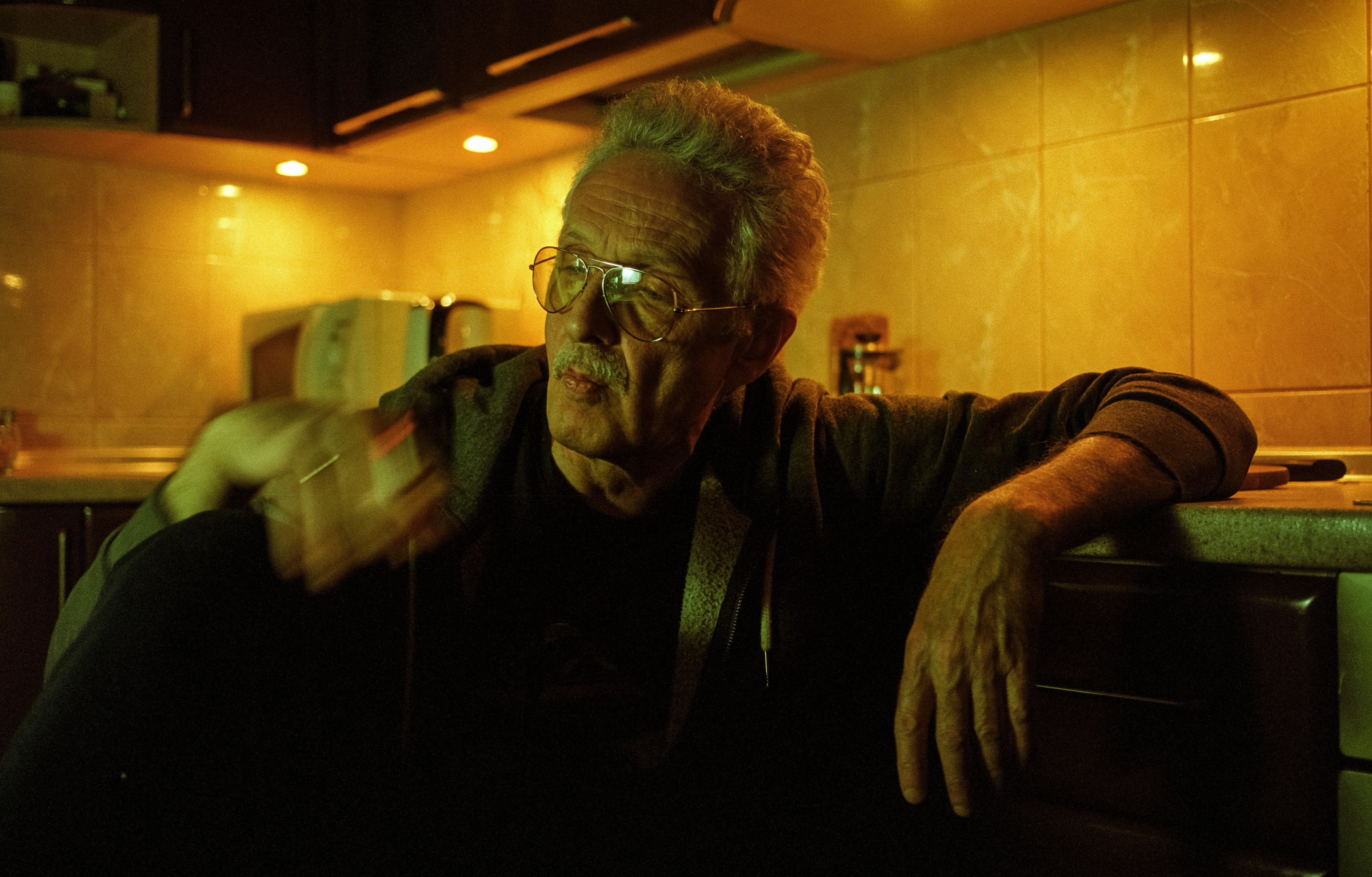 A man sitting in a kitchen next to a stove top oven