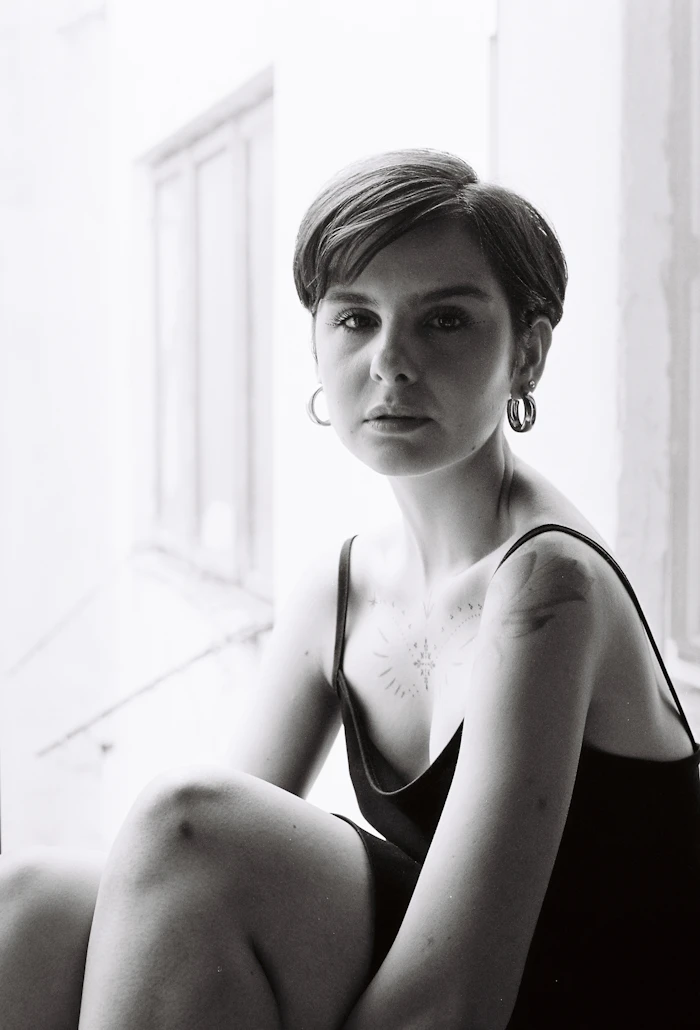 A woman with a short, cropped haircut sitting by a bright window