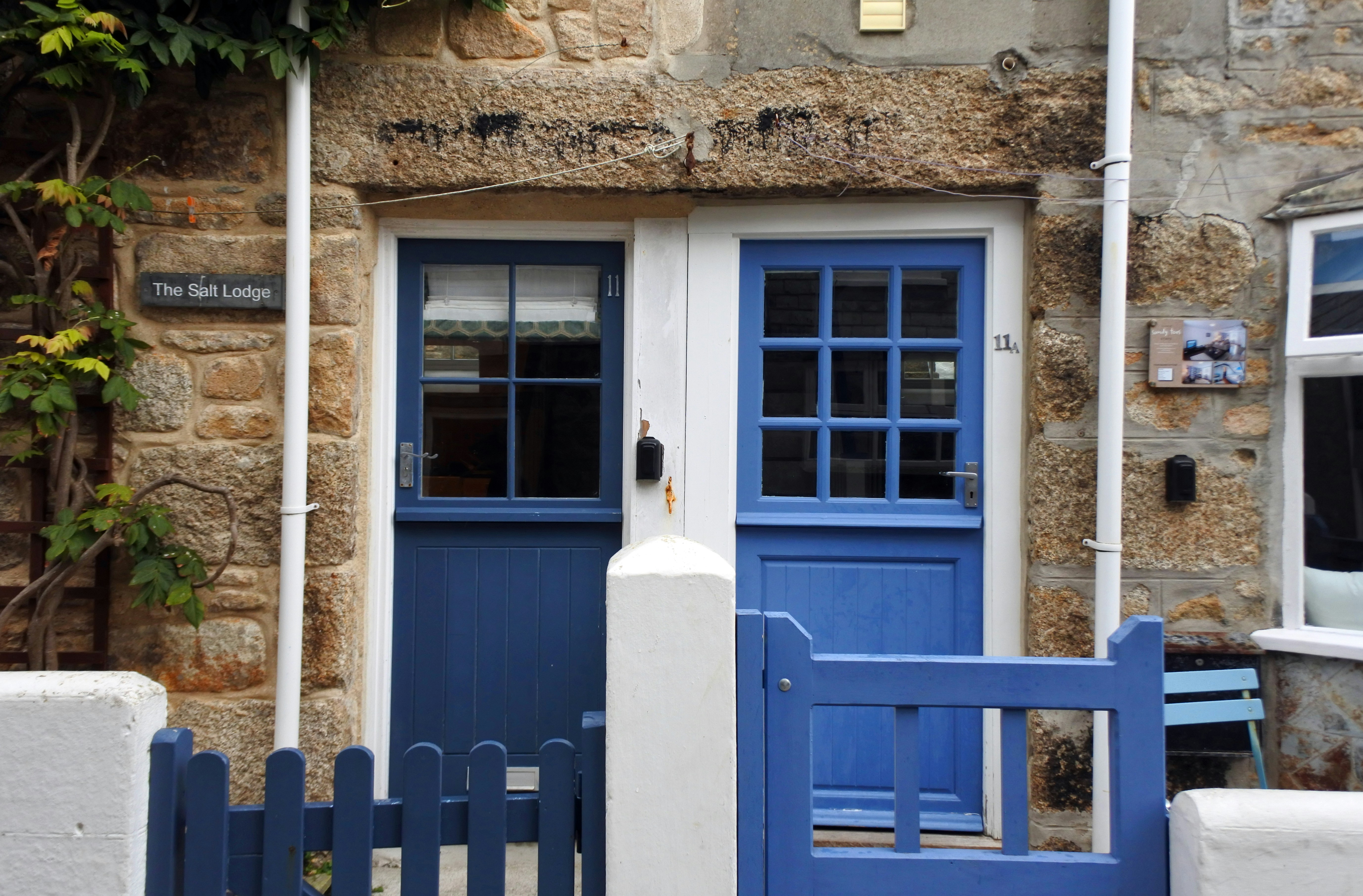 Una puerta azul y una valla blanca frente a un edificio de piedra