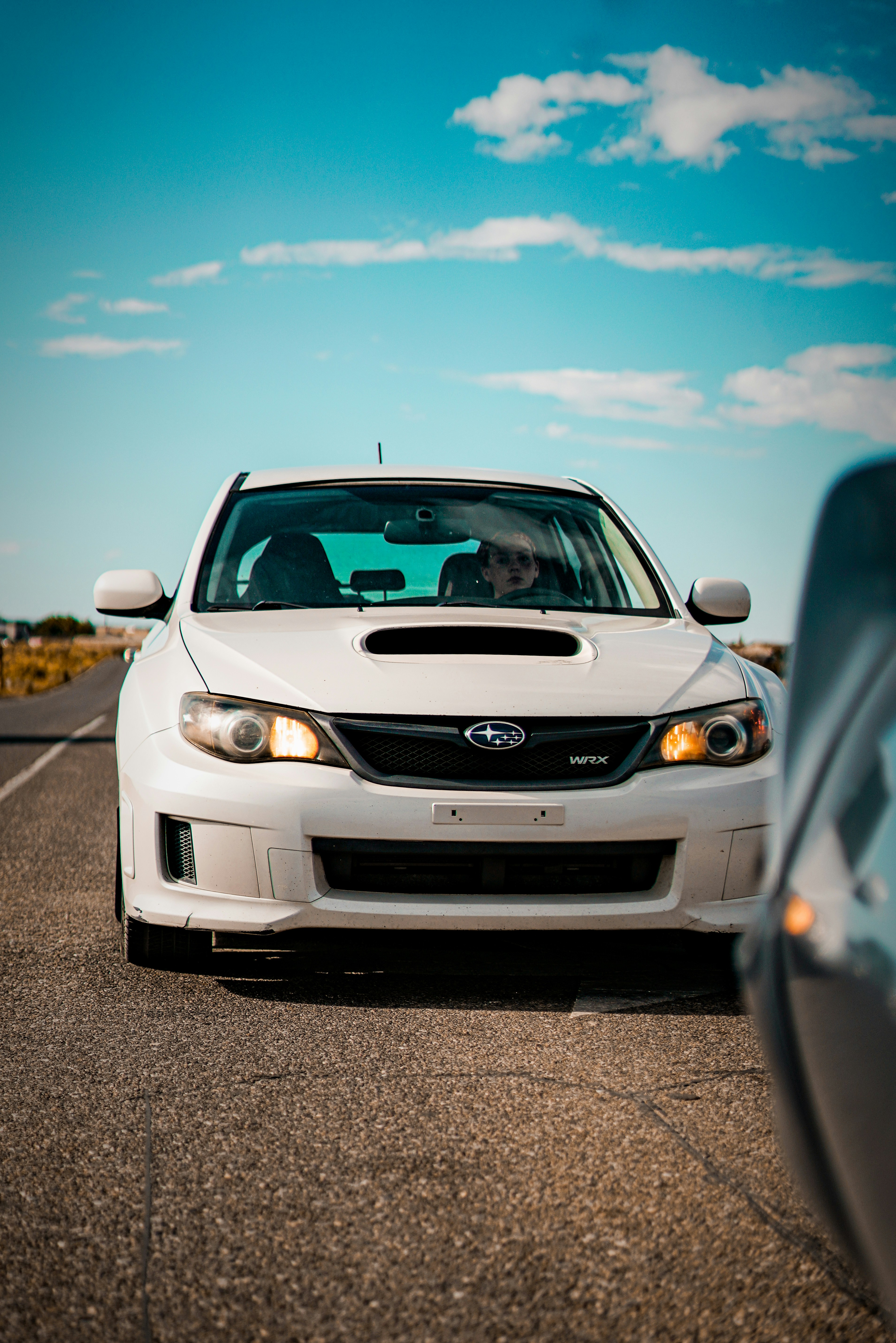 A white car driving down a road next to a blue sky