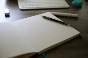 A notebook with a pen on top of it next to a keyboard