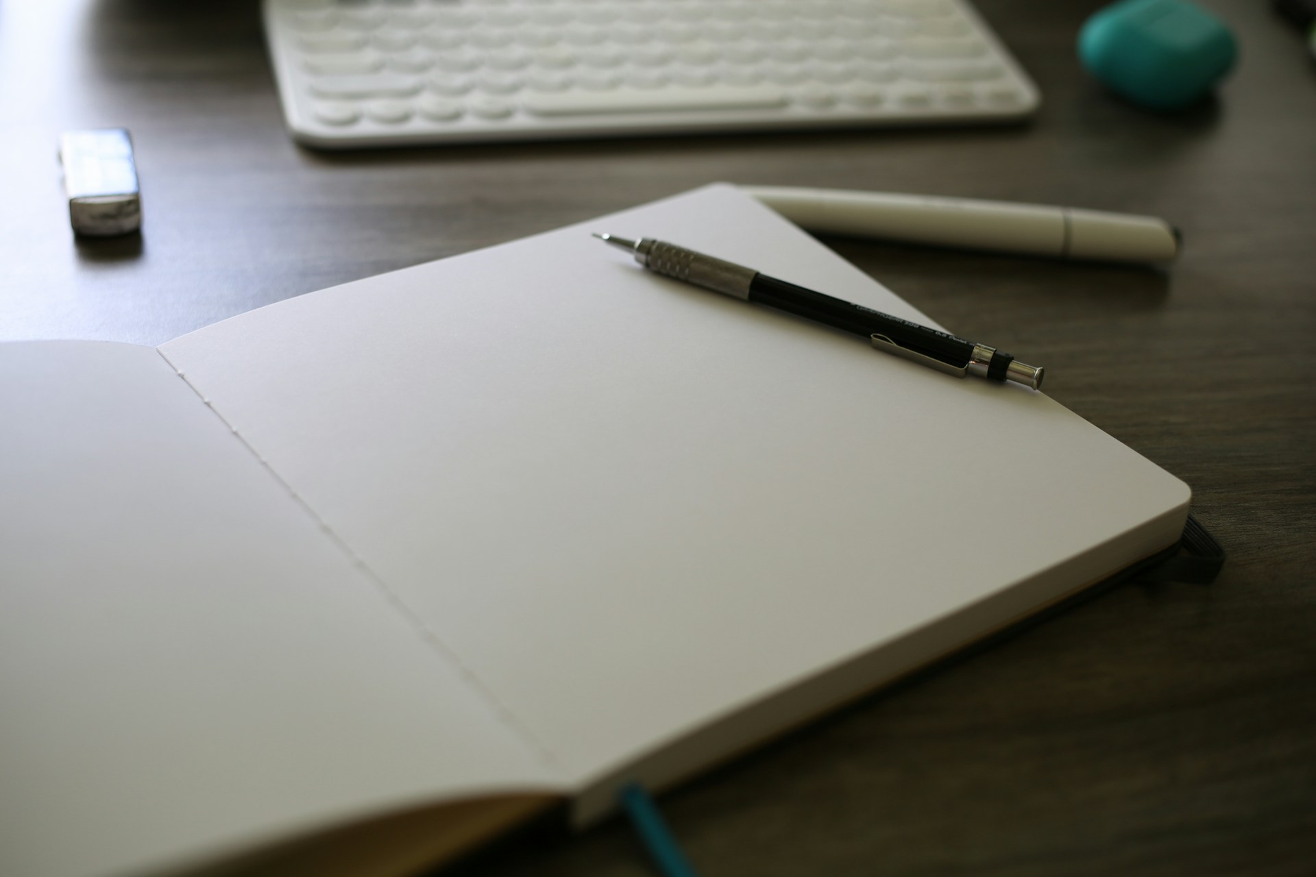 A notebook with a pen on top of it next to a keyboard