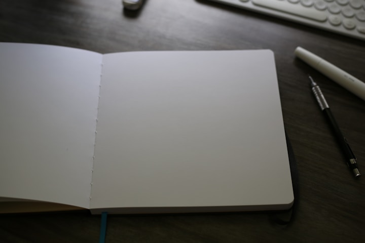 An open notebook sitting on a desk next to a keyboard