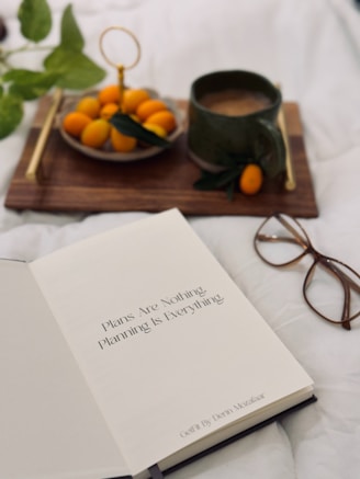 An open book sitting on top of a bed next to a bowl of fruit
