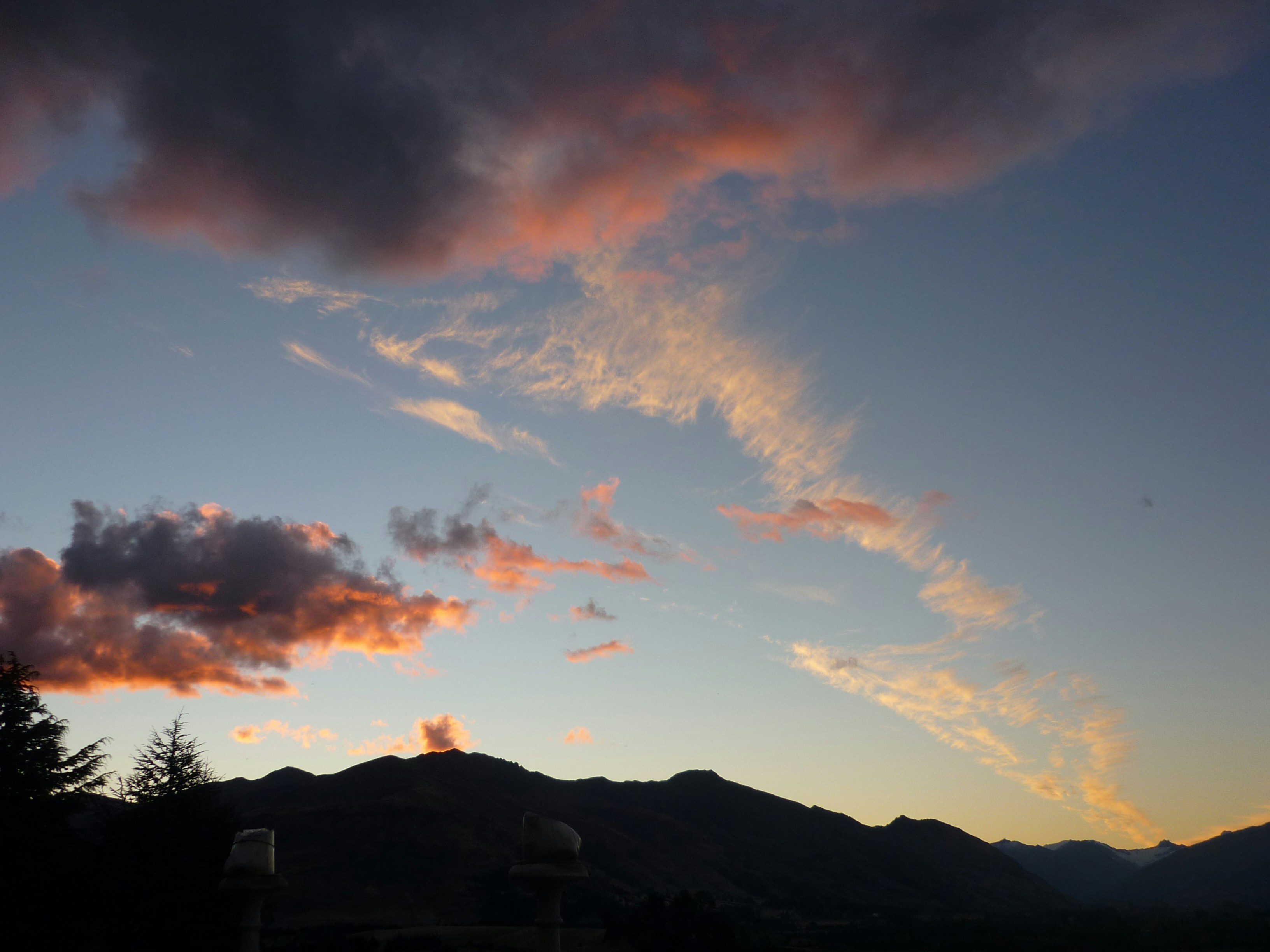 A view of a sunset with clouds and mountains in the background
