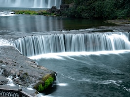 A waterfall with a bridge over it next to a body of water
