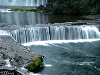 A waterfall with a bridge over it next to a body of water
