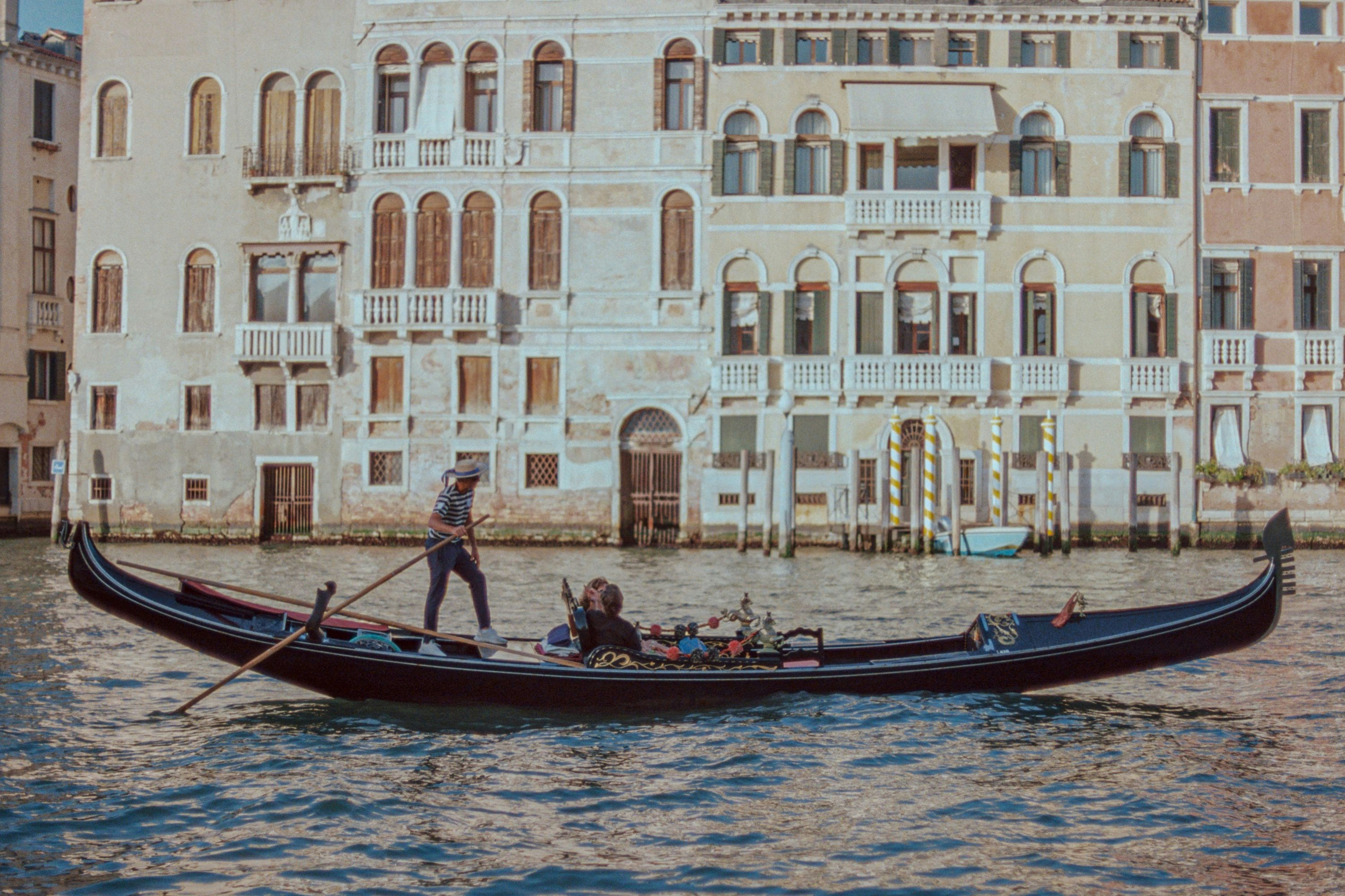 A man riding a boat down a river next to tall buildings photo – Free ...