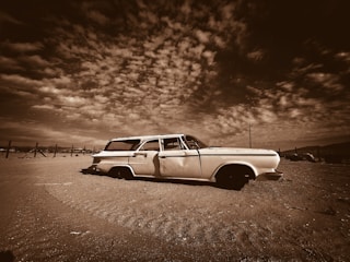 An old car parked in a field under a cloudy sky
