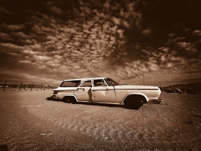 An old car parked in a field under a cloudy sky