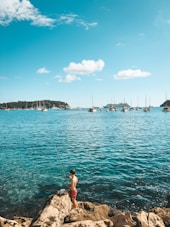 A young boy standing on a rock next to a body of water