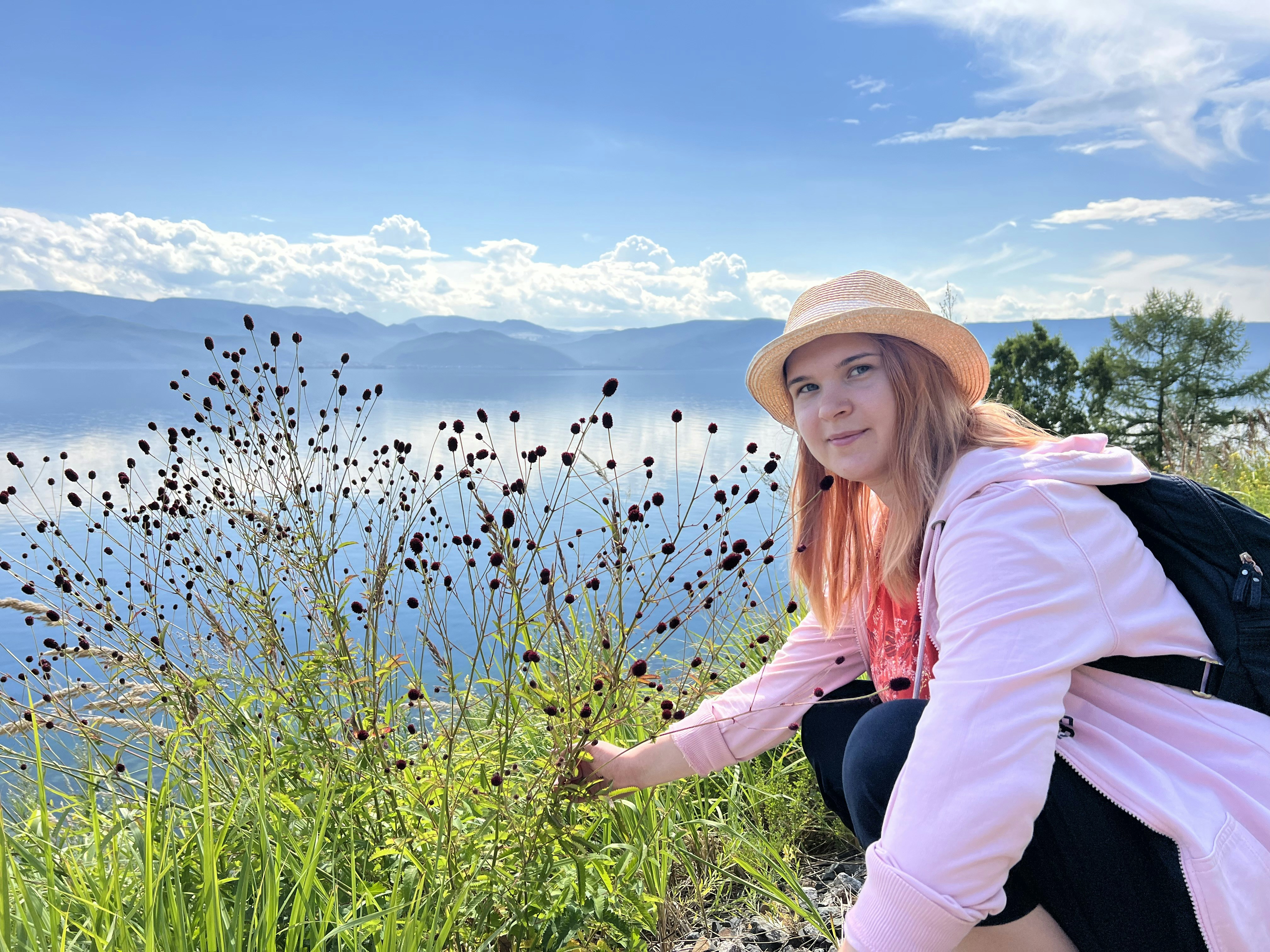 A woman in a hat crouches on the edge of a cliff