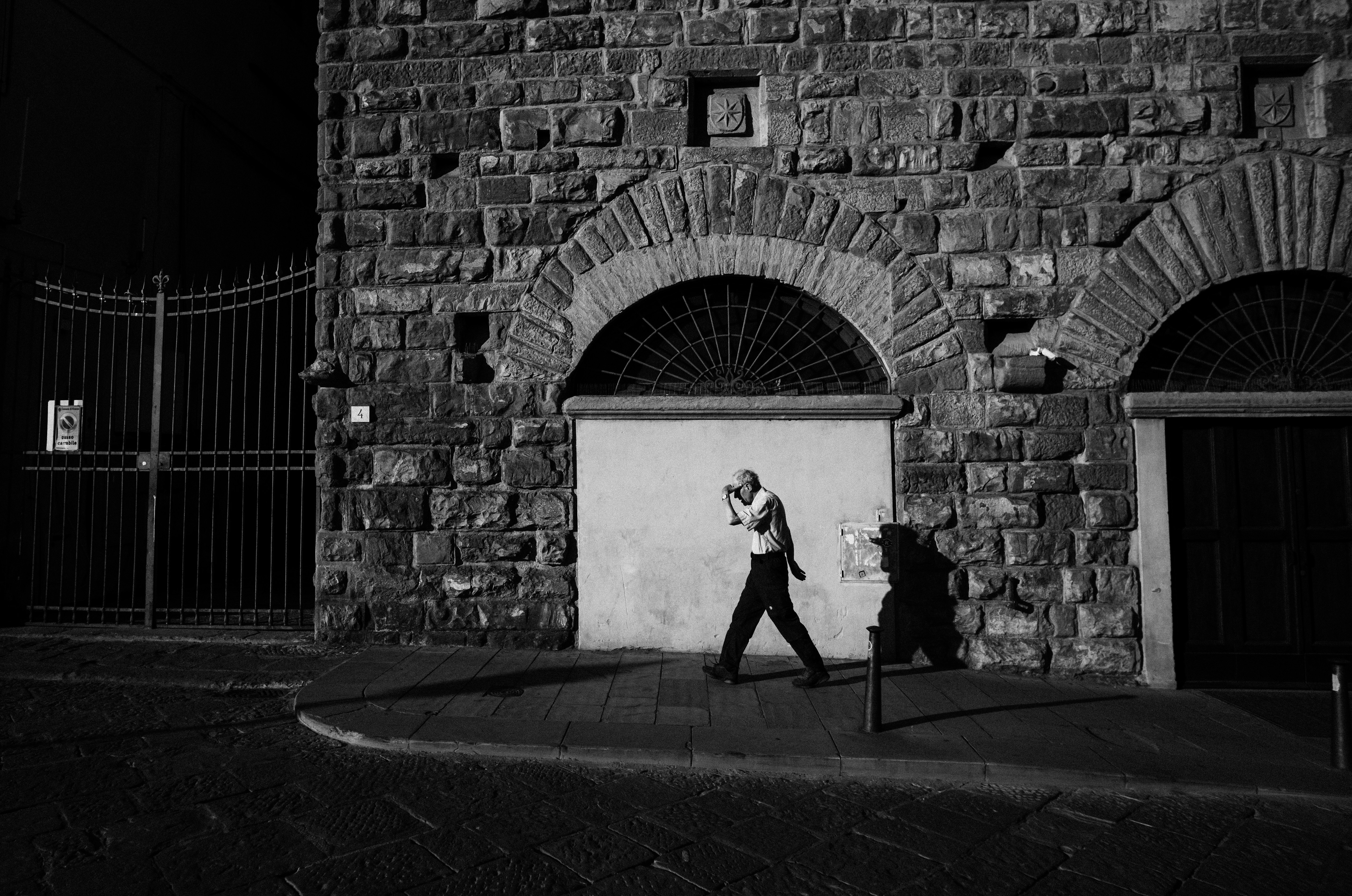 A black and white photo of a man walking past a building