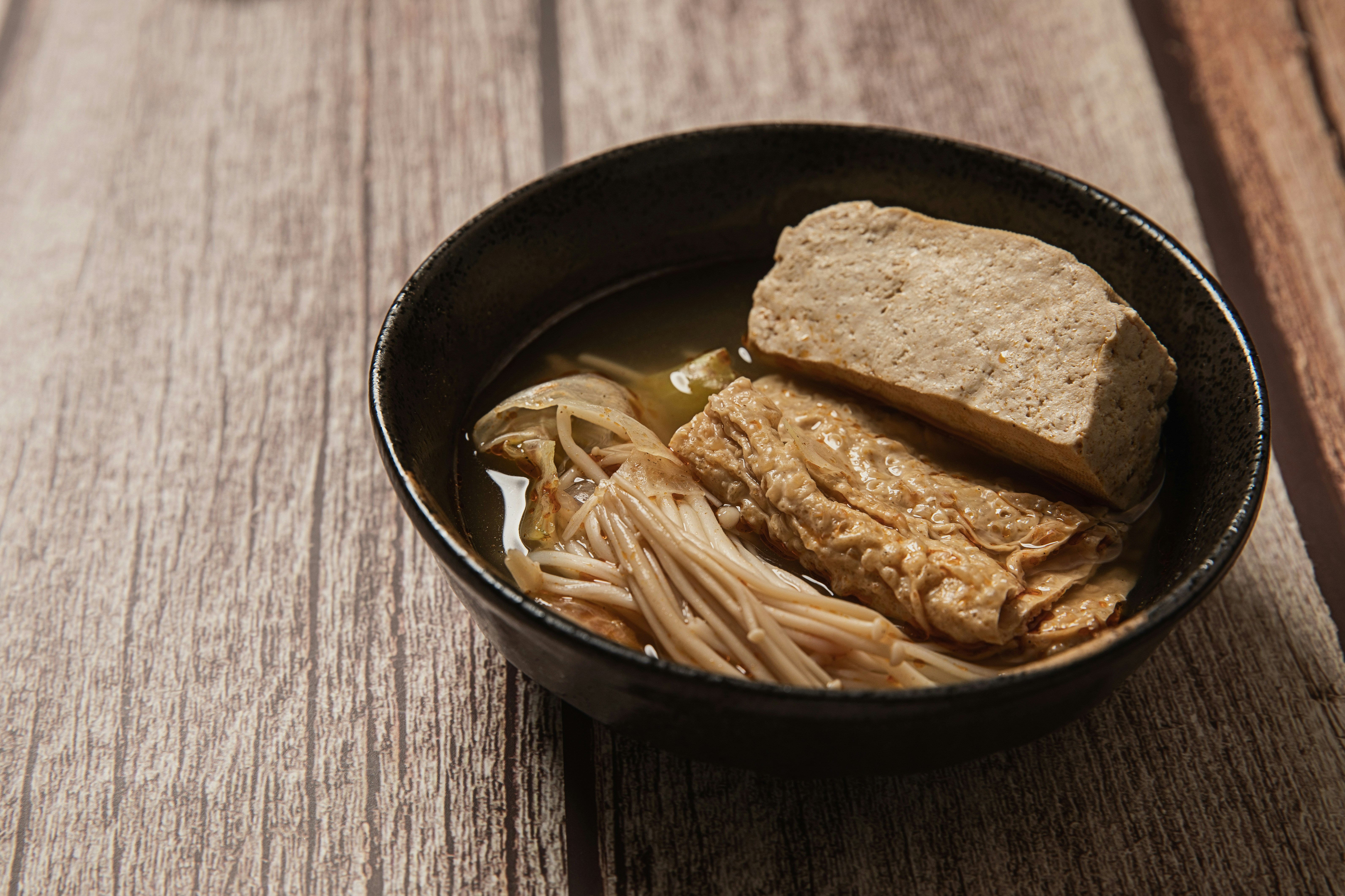 Small bowl of clear miso soup with tofu cubes and green onions, minimalist dark wooden table