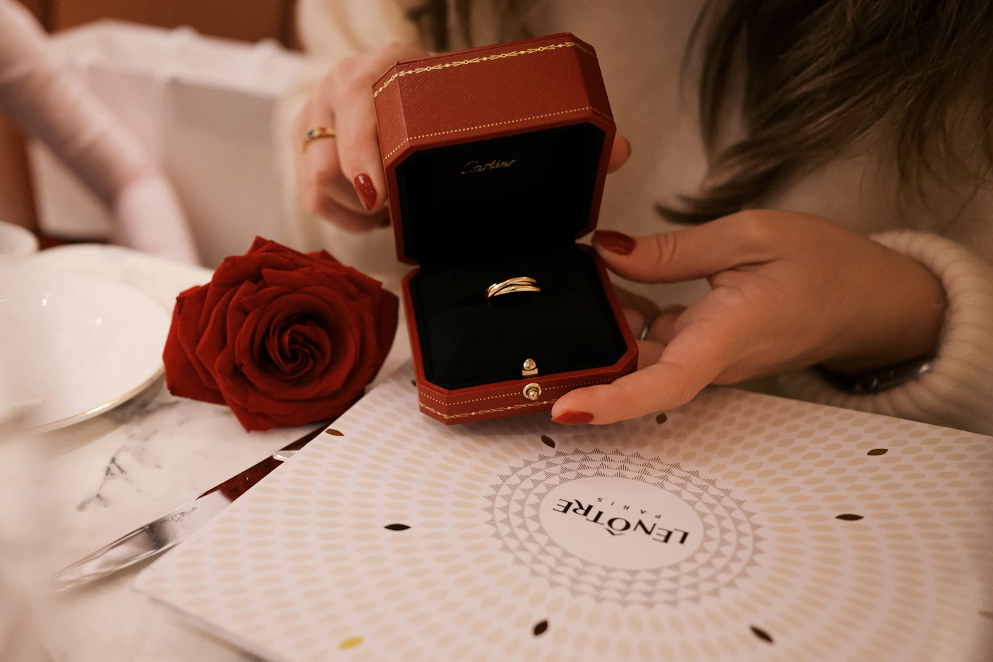 A woman sitting at a table holding a ring box