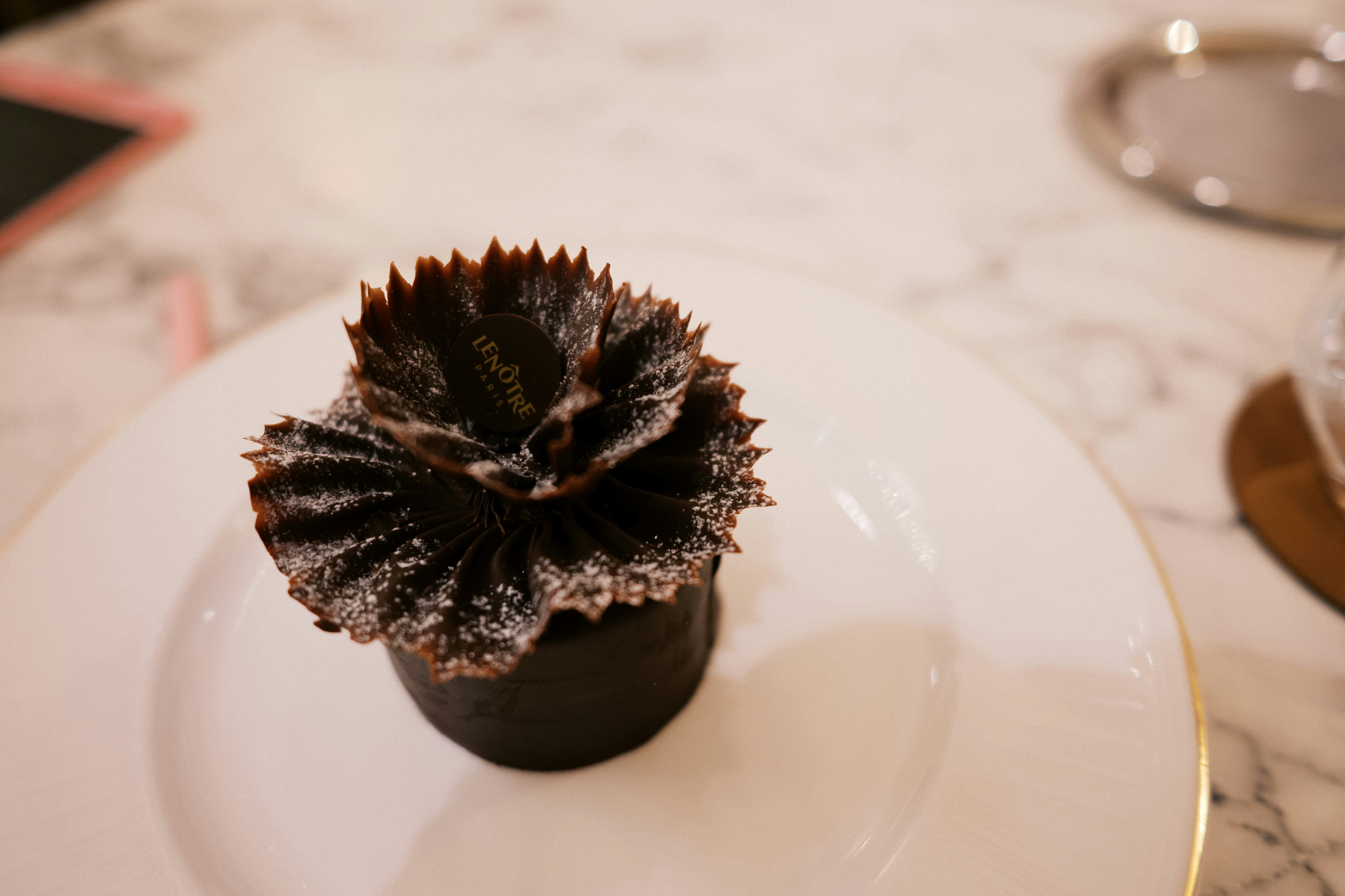 A white plate topped with a chocolate cupcake, French desert by Le Nôtre