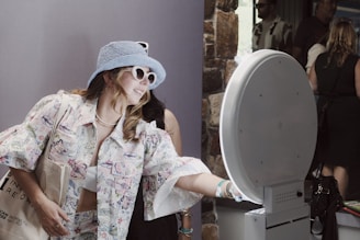 A woman wearing a blue hat and sunglasses standing next to a toilet