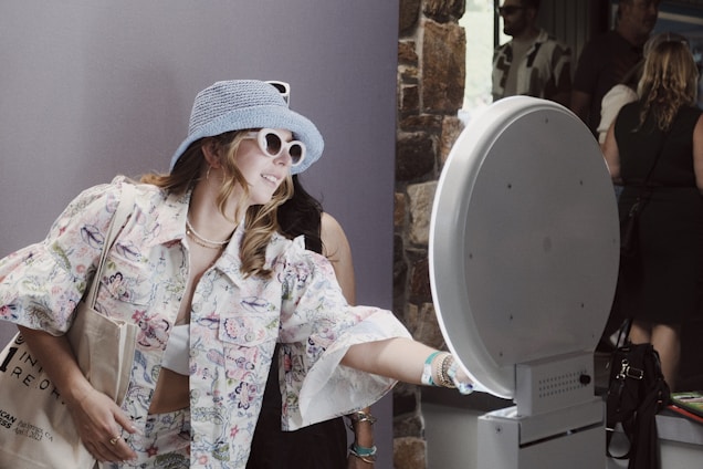 A woman wearing a blue hat and sunglasses standing next to a toilet