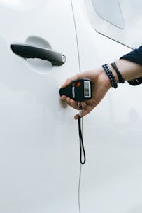 A hand holding a remote control near a white car