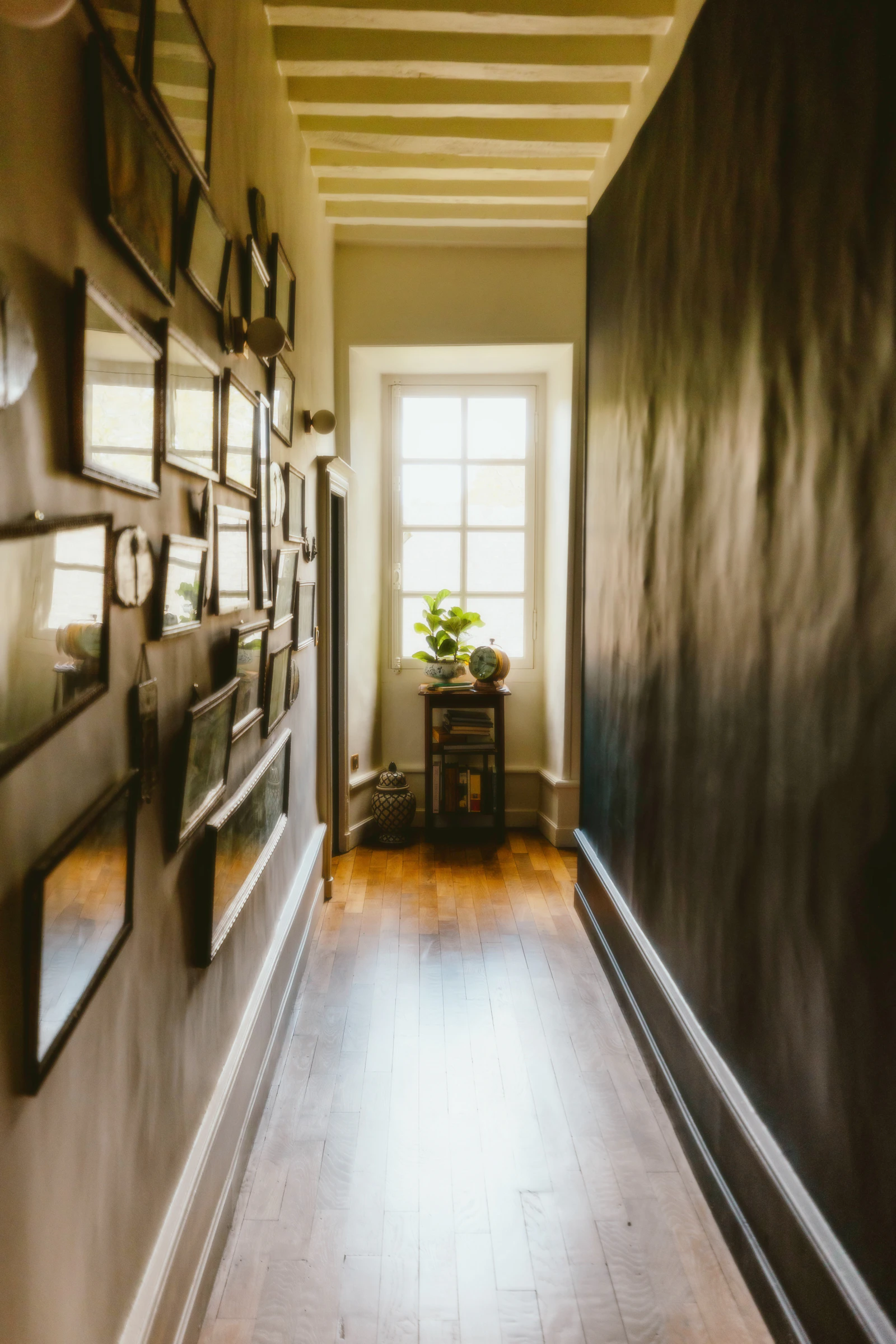 A long hallway with a dark painted feature wall, white skirting boards and framed artwork.