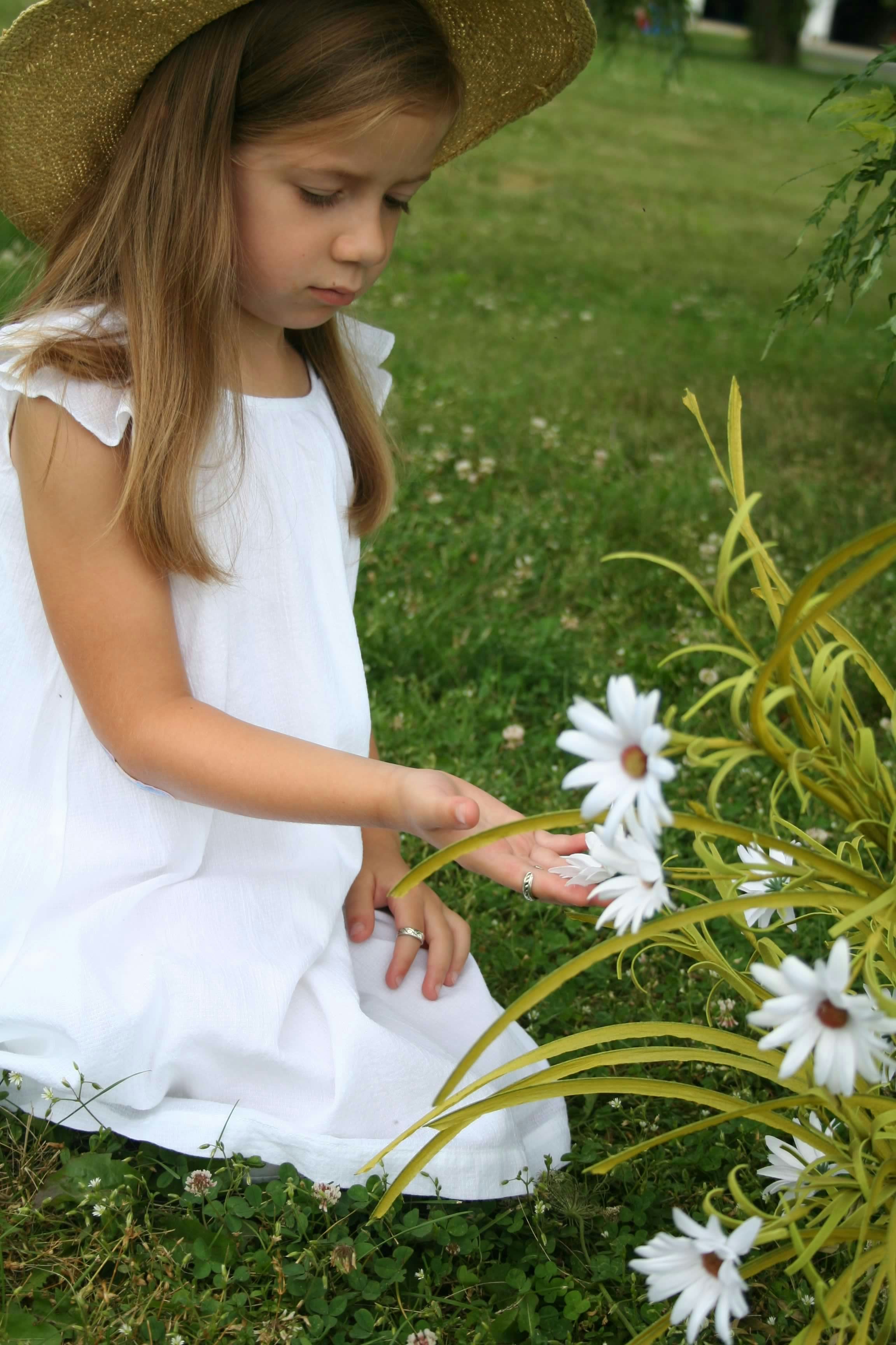 A little girl sitting in the grass next to a flower