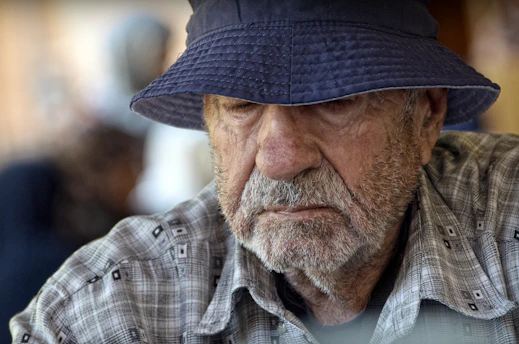 An old man wearing a hat and looking at the camera