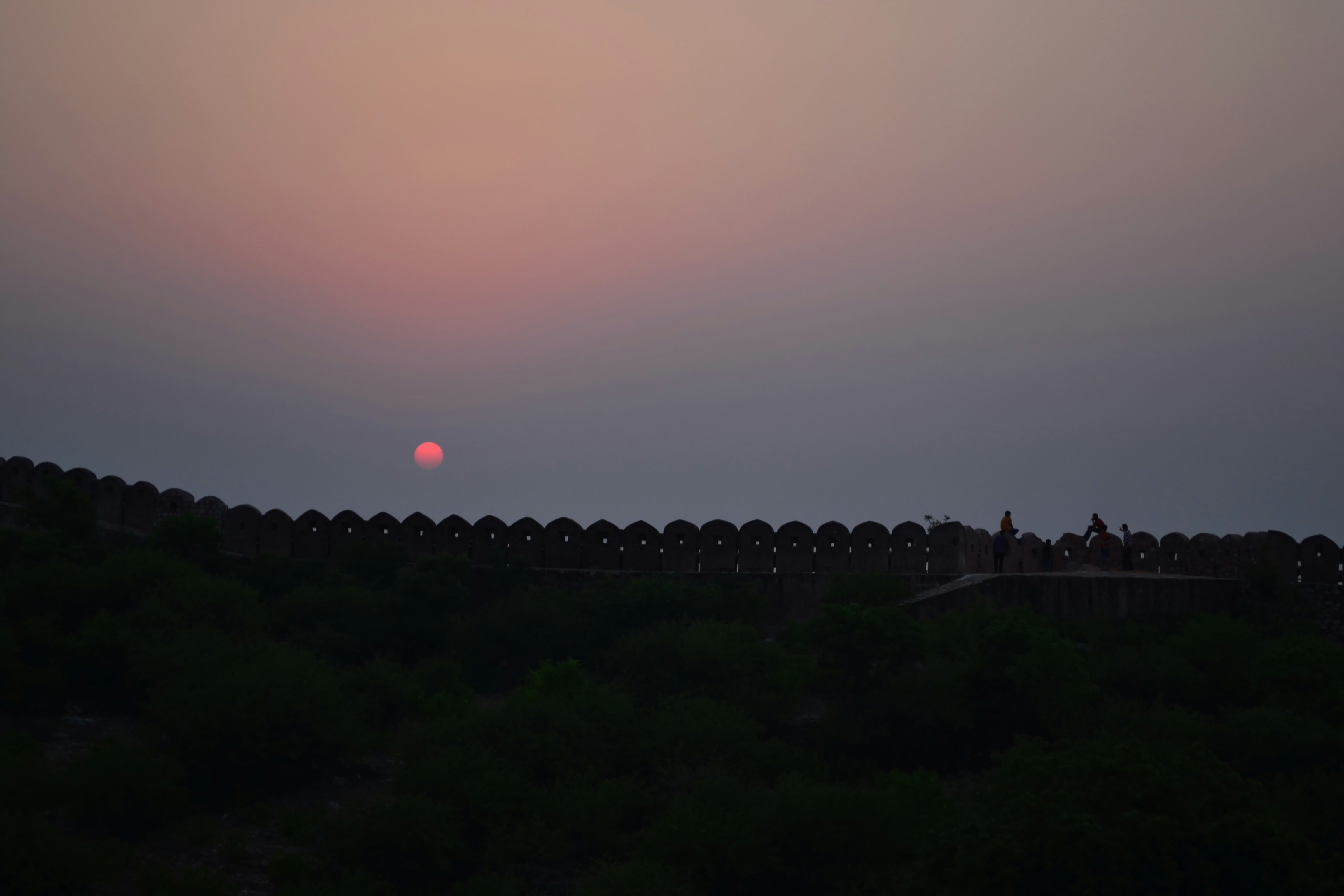 The sun is setting over a hill with trees
