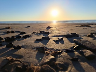 The sun is setting over a beach with rocks