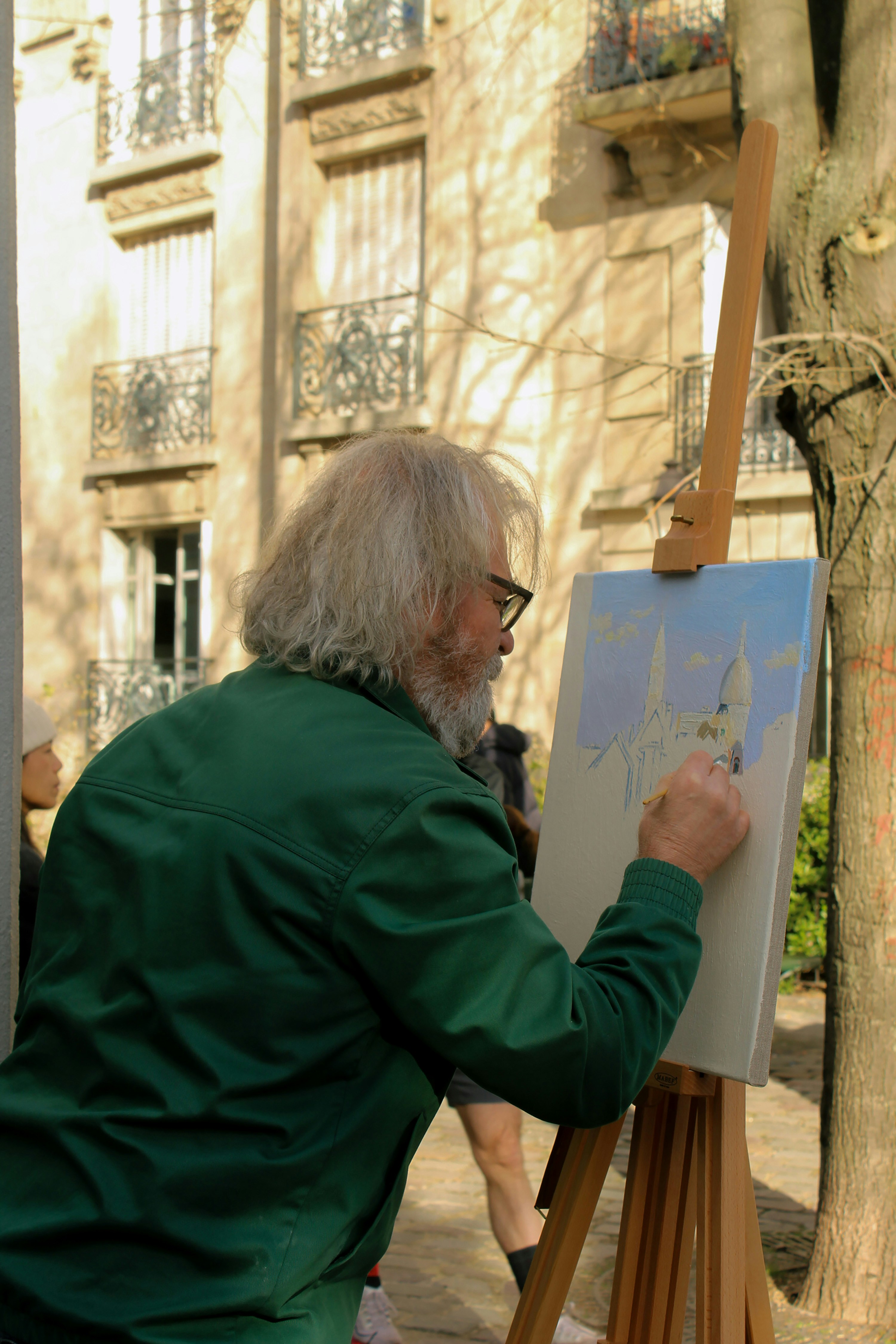 A man is painting on a easel in front of a building
