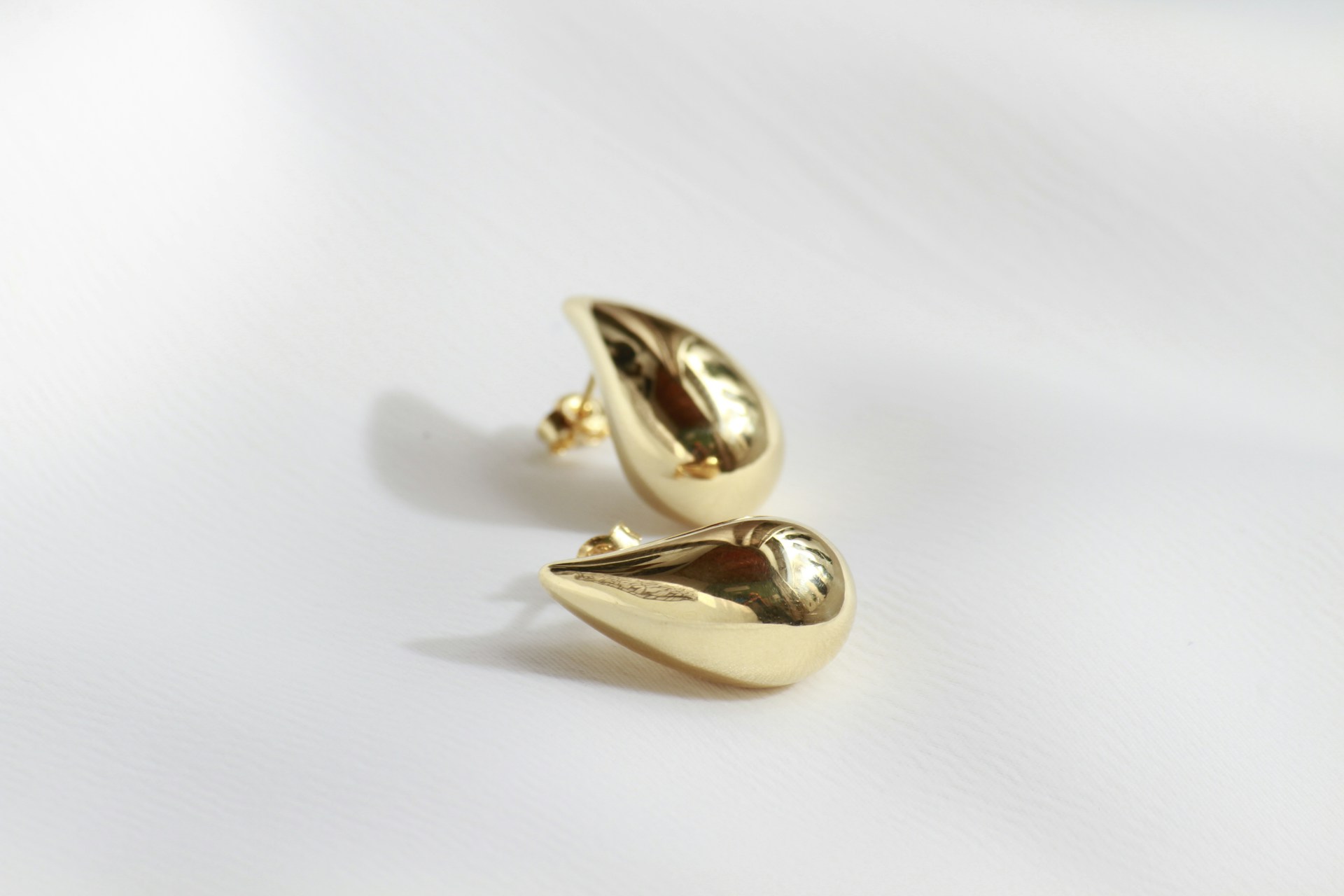 A pair of gold earrings sitting on top of a white surface