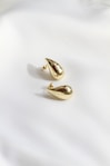 A pair of gold earrings sitting on top of a white sheet