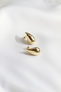 A pair of gold earrings sitting on top of a white sheet