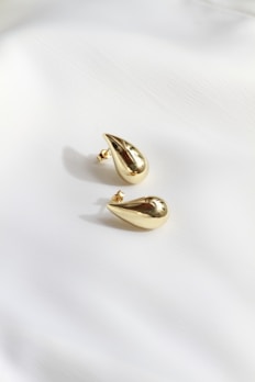 A pair of gold earrings sitting on top of a white sheet