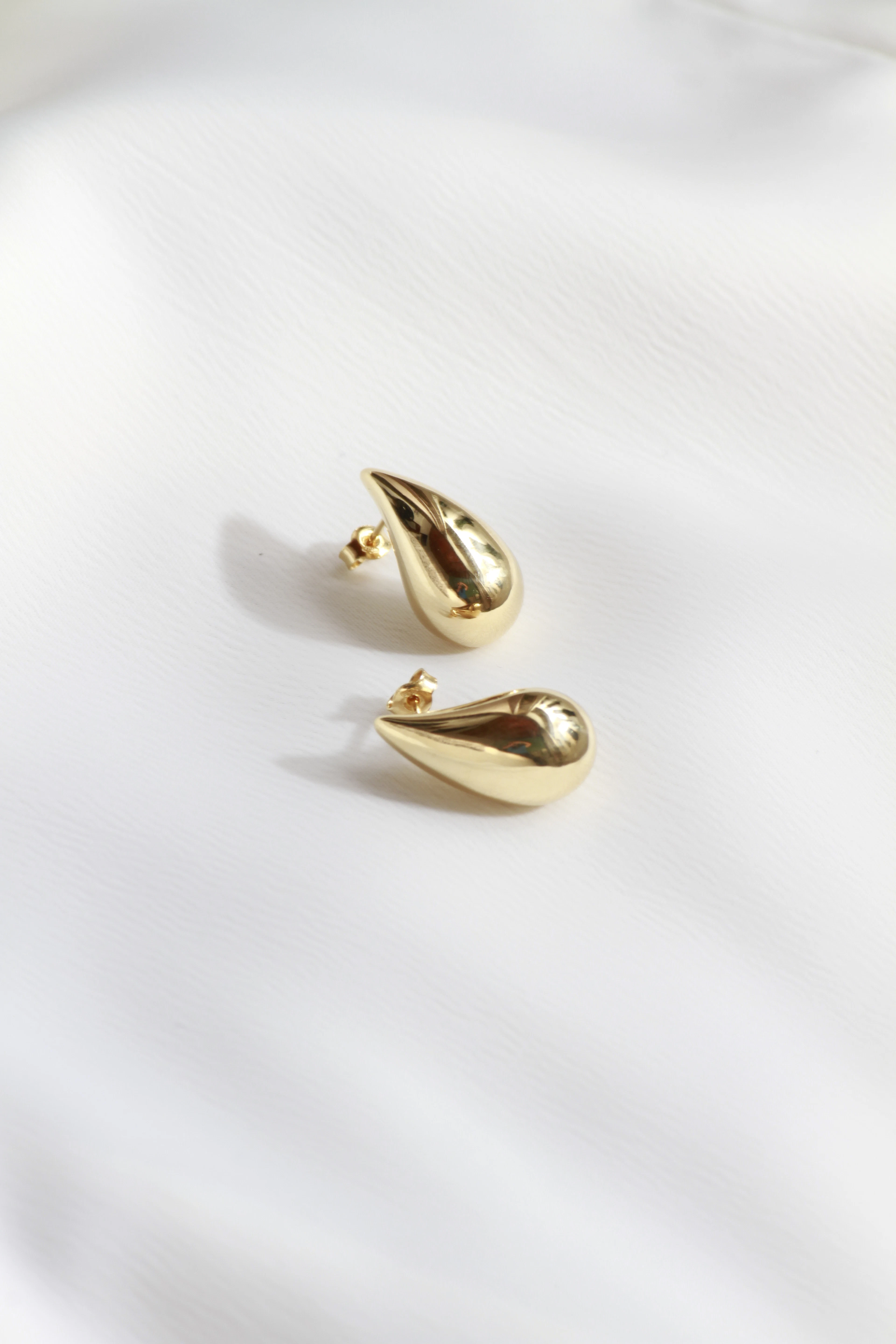 Pair of sculpted gold teardrop earrings resting on white linen