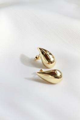 A pair of gold earrings sitting on top of a white sheet