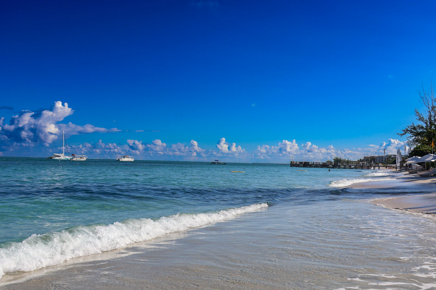 Turks and Caicos beach in the morning with a boat anchored offshore and the turquoise water reflecting the clear sky with white sand beach in the foreground