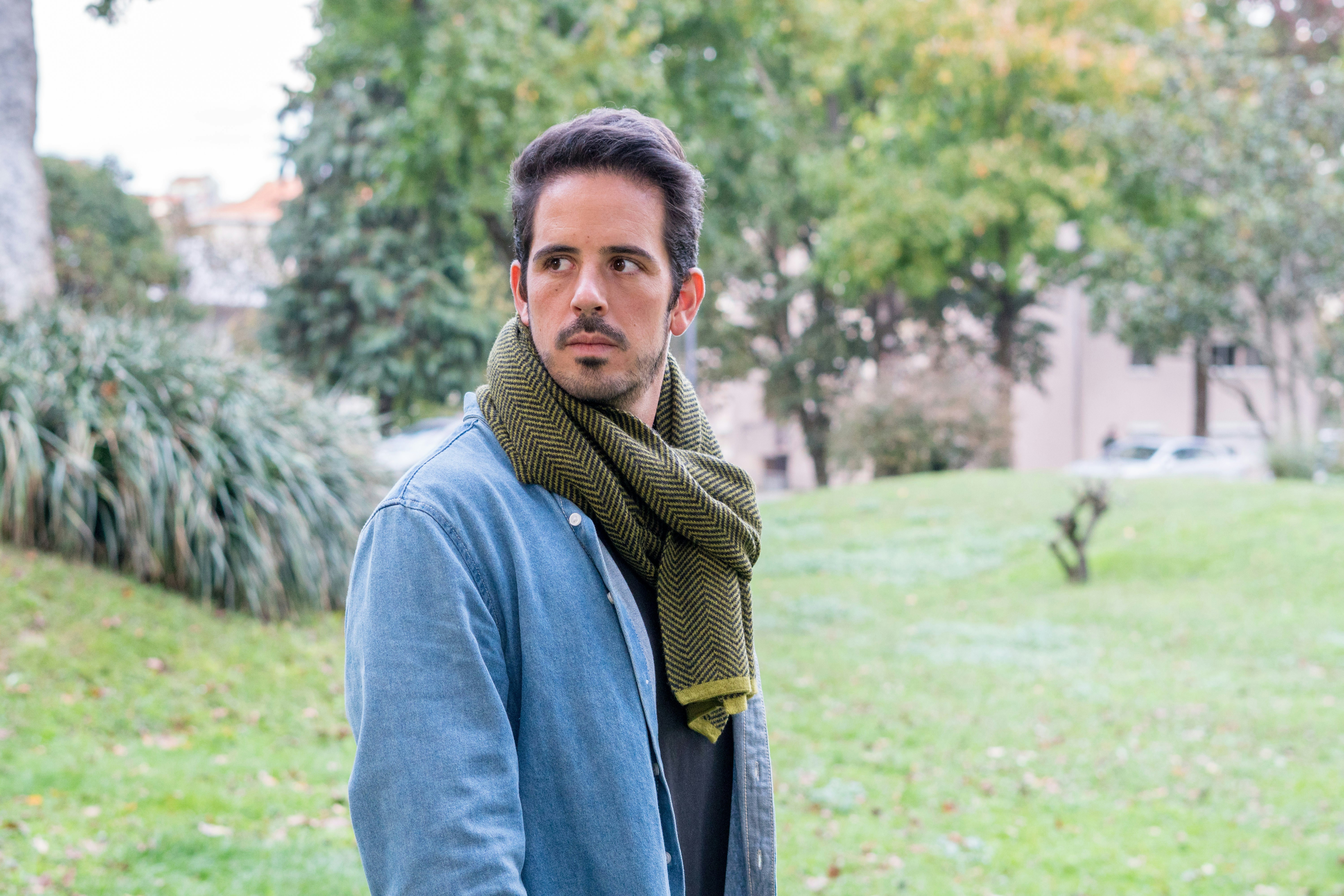 A man standing in a park with a scarf around his neck