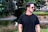 A man in a black t - shirt is holding a skateboard