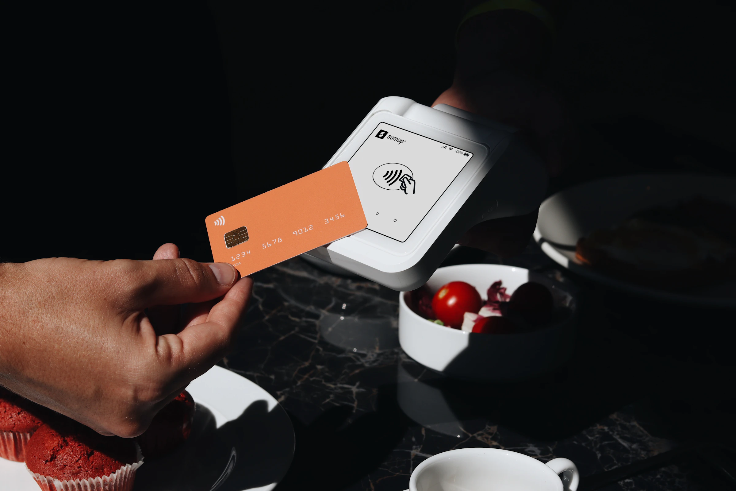 A diner holding a bank card to a handheld card machine at a restaurant table set with small dishes