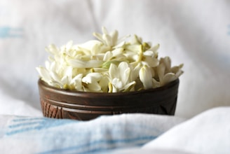 A wooden bowl filled with white flowers on top of a bed