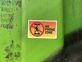 A no phone zone sign on a green wall