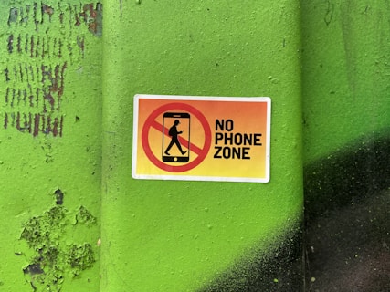 A no phone zone sign on a green wall