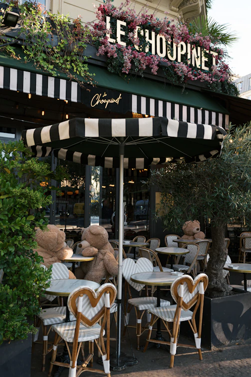 A teddy bear sitting at a table in front of a restaurant