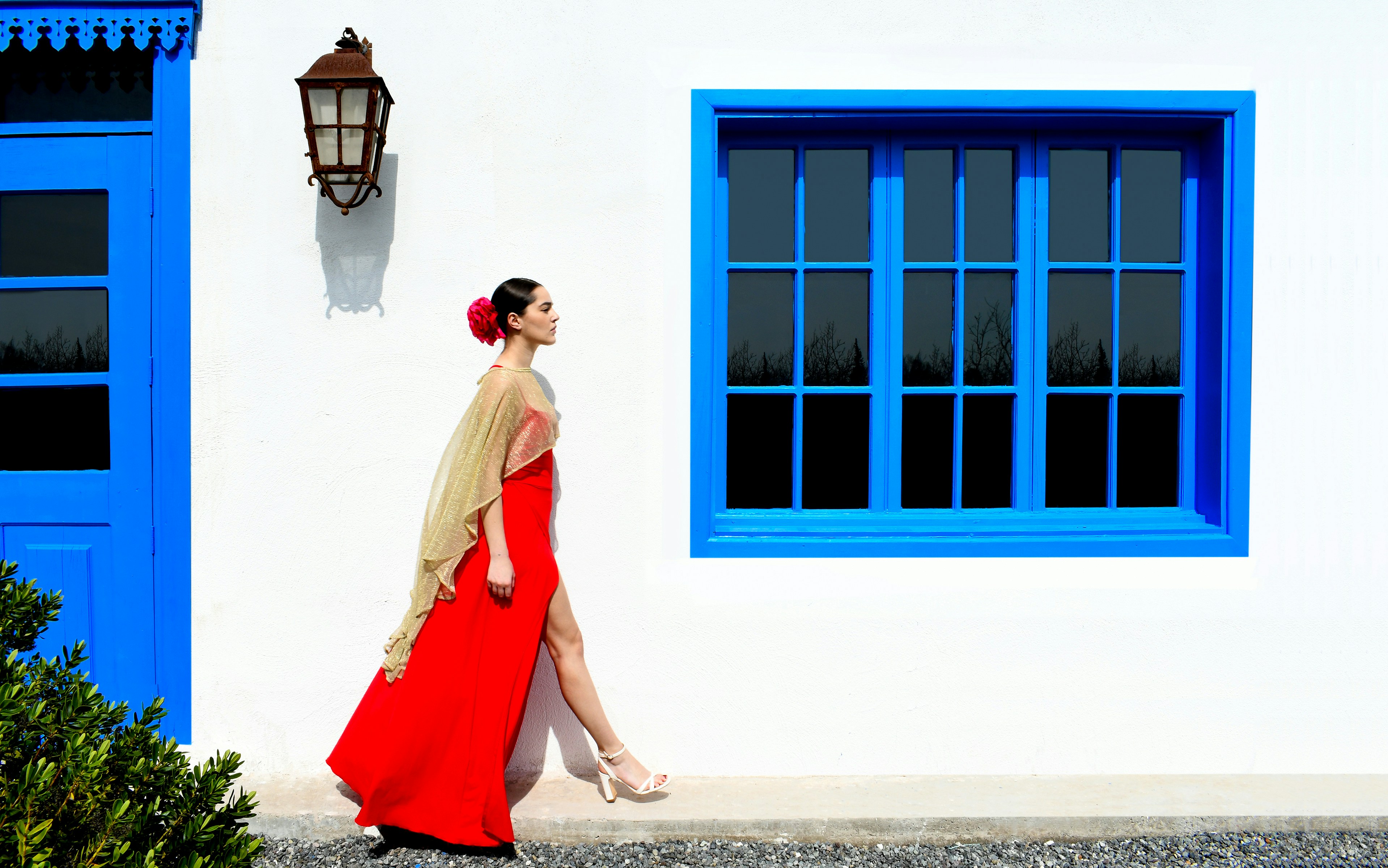 白い建物の前を歩く赤いドレスの女性